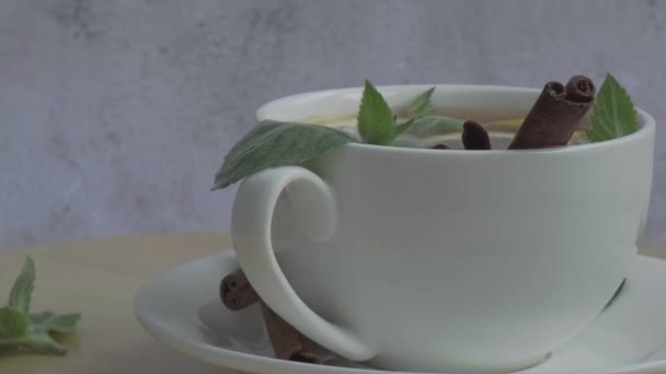 Черный и зеленый чай с лимоном, палочками корицы и листьями мяты вращающимися. Горячий напиток Здоровый чай Мелисса натуральный органический ароматический напиток в чашке. Лето, осень и зима. — стоковое видео