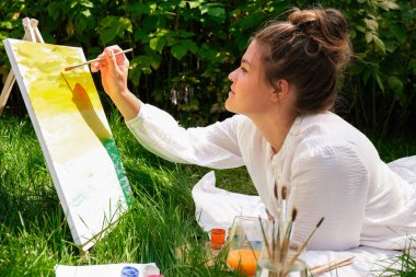 Bahçedeki sehpada ressam resmi. Açık hava sanat atölyesi. Parktaki bir piknik sırasında çimlerin üzerine fırça ve paletle resim çiz.