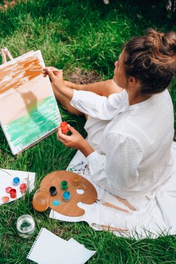 Bahçedeki sehpada ressam resmi. Açık hava sanat atölyesi. Parktaki bir piknik sırasında çimlerin üzerine fırça ve paletle resim çiz.