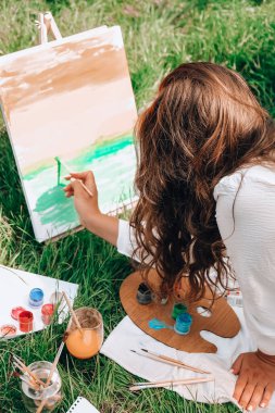 Bahçedeki sehpada ressam resmi. Açık hava sanat atölyesi. Parktaki bir piknik sırasında çimlerin üzerine fırça ve paletle resim çiz.