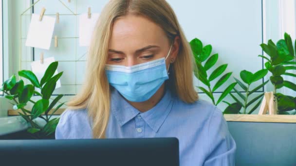 Een jonge vrouw werkt op een computer in een modern kantoor. Zakenvrouw die aan haar laptop werkt met een medisch gezichtsmasker. Online conferentie bijles. Online onderwijs student — Stockvideo