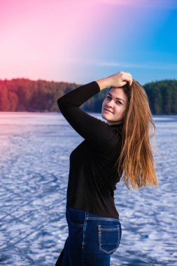 Genç bir bayan gülümsüyor ve kar manzarasında bir kameraya bakıyor. Hip hop ile sıcak kış kıyafetleri giyen mutlu hippi kız. Donmuş nehirde, gölde kalıyorum. Çekici, gülümseyen bir kadının kış portresi.