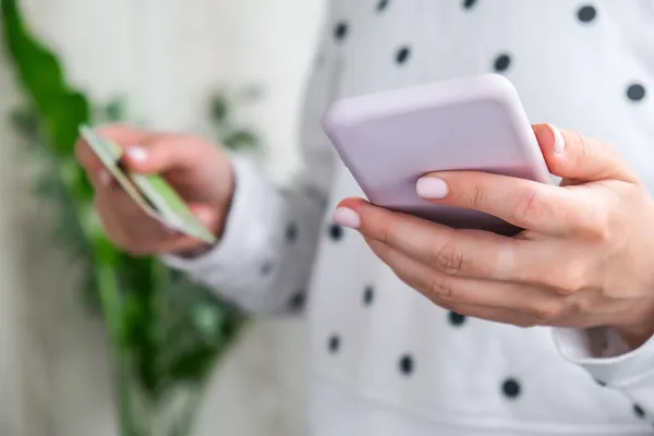 Close up view of female using online banking application on smartphone and holding debit credit card at home. Online shopping. Stay home