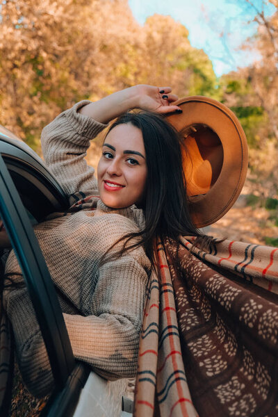 Brunette European looking cute girl sitting in a car enjoying sunny autumn weekend. Travel and road trip. Woman looking at the view from a car. Happy woman enjoying road trip