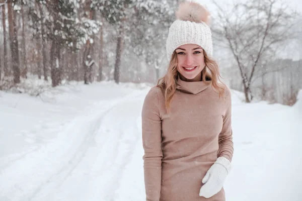 Navidad, vacaciones y concepto de temporada. Joven mujer feliz soplando nieve en la naturaleza del bosque de invierno. Ropa de abrigo guantes de punto y sombrero. — Foto de Stock