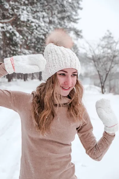 Natal, feriados e conceito de temporada. Jovem mulher feliz soprando neve na natureza da floresta de inverno. Roupas quentes luvas de malha e chapéu. — Fotografia de Stock