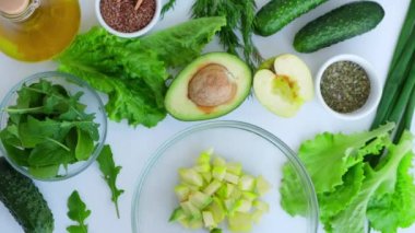 Taze yeşil sebze ve ottan salata pişiren bir kadın. Çiğ gıda konsepti. Vejetaryen menüsü. Sağlıklı beslenme ya da vejetaryen yemekleri pişirmek. Kadın eli kesme tahtasının üzerinde yeşil sebzelerle çevrili avokado.