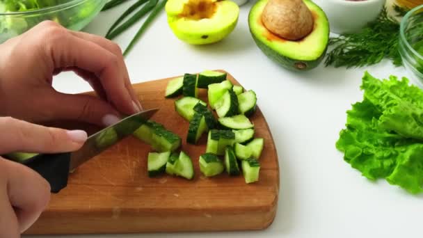 新鮮な緑の野菜やハーブの女性の料理サラダ。生食の概念。ビーガンメニュー。健康的な食事やベジタリアン料理を調理します。女性の手は緑に囲まれたまな板にキュウリをカット — ストック動画