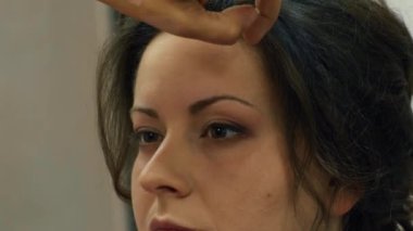 Saç spreyli saç stili, balo hazırlığı. Güzellik salonunda tanınmayan bir kadının uzun saçları için saç maşası kullanan kuaförünün yakın plan görüntüsü..