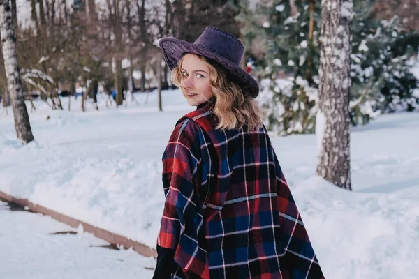 Kar parkında kış havasının tadını çıkaran genç bir kadın. Soğuk hava. Kış modası, tatiller, dinlenme, seyahat konsepti. Kovboy şapkası ve panço. — Stok fotoğraf
