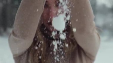 Noel, tatiller ve kış mevsimi konsepti. Genç mutlu kadın kış ormanlarında karla oynarken esiyor. Yavaş çekim, kalın kıyafetler, örgü eldivenler ve şapka..