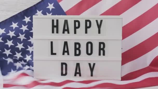 Im Hintergrund weht die amerikanische Flagge in Zeitlupe. Leuchtkasten mit Text HAPPY LABOR DAY Flagge der Vereinigten Staaten von Amerika. 4. Juli, Unabhängigkeitstag. Nationalfeiertag des Patriotismus in den USA. USA stolz. — Stockvideo