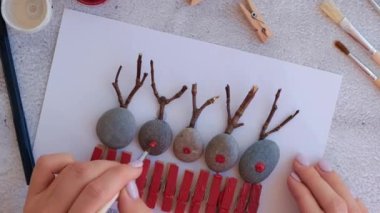 Çakıl taşları, deniz taşları, çamaşır mandalları ve beyaz arka planda dallardan oluşan kartpostalda Mutlu Noeller geyiği yapmak. Doğal Eko tarzı diy. Hediye fikri. Adım adım. Üst görünüm.