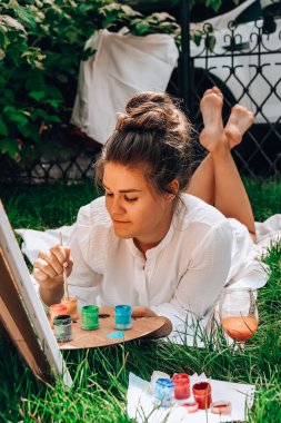 Bahçedeki sehpada ressam resmi. Açık hava sanat atölyesi. Parktaki bir piknik sırasında çimlerin üzerine fırça ve paletle resim çiz.