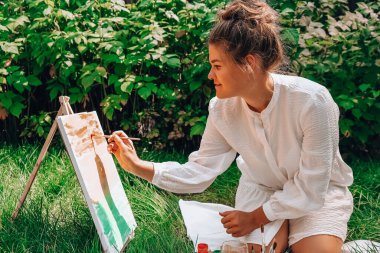 Bahçedeki sehpada ressam resmi. Açık hava sanat atölyesi. Parktaki bir piknik sırasında çimlerin üzerine fırça ve paletle resim çiz.