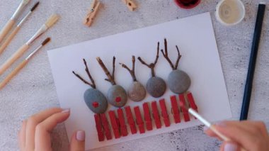 Çakıl taşları, deniz taşları, çamaşır mandalları ve beyaz arka planda dallardan oluşan kartpostalda Mutlu Noeller geyiği yapmak. Doğal Eko tarzı diy. Hediye fikri. Adım adım. Üst görünüm.