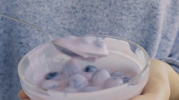 Miska z jogurtem i jagodami na stole. Kobieta je jogurt jagodowy ze świeżymi jagodami. Zdrowe śniadanie. Super jedzenie zdrowe jedzenie wegetariańskie jedzenie wegańskie — Wideo stockowe