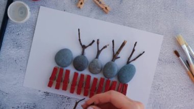Çakıl taşları, deniz taşları, çamaşır mandalları ve beyaz arka planda dallardan oluşan kartpostalda Mutlu Noeller geyiği yapmak. Doğal Eko tarzı diy. Hediye fikri. Adım adım. Üst görünüm.