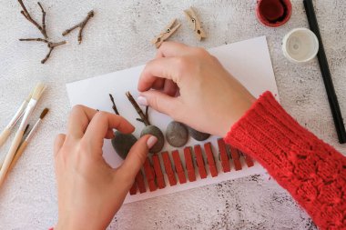 Adım adım. Üst Manzara. İşlemci çocuk işi. Kendin yap Mutlu Noeller geyiği çakıl taşlarından, deniz taşlarından, mandallardan ve beyaz arka planda dallardan oluşan kartpostalda. Doğal Eko tarzı diy. Hediye fikri..