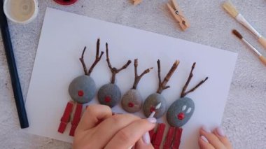 Çakıl taşları, deniz taşları, çamaşır mandalları ve beyaz arka planda dallardan oluşan kartpostalda Mutlu Noeller geyiği yapmak. Doğal Eko tarzı diy. Hediye fikri. Adım adım. Üst görünüm.