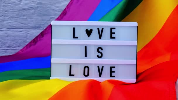 라이트 박스와 텍스트 LOVE 는 사랑이다 라는 문구가 적힌 4k 무지개 깃발. 레인보우 lgbtq 플래그는 실크 재료로 만들어 졌다. 성 소수자의 상징성은 성 소수자의 달을 의미 한다. 동등 한 권리. 평화와 자유 — 비디오