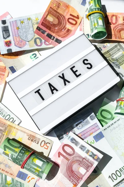 Lightbox board com palavra TAXES em letras pretas em torno de notas de euro. Pagamento de impostos e conceito de depósito. Dinheiro, Negócios, Finanças, Investimento, Economia e Corrupção — Fotografia de Stock
