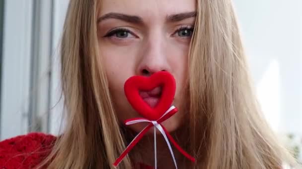 Jeune fille blonde en pull rouge tenant des cœurs rouges montrant des émotions. Appel vidéo. Saint Valentin. L'amour au loin. Reste à la maison — Video