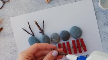 Çakıl taşları, deniz taşları, çamaşır mandalları ve beyaz arka planda dallardan oluşan kartpostalda Mutlu Noeller geyiği yapmak. Doğal Eko tarzı diy. Hediye fikri. Adım adım. Üst görünüm.