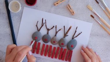 Çakıl taşları, deniz taşları, çamaşır mandalları ve beyaz arka planda dallardan oluşan kartpostalda Mutlu Noeller geyiği yapmak. Doğal Eko tarzı diy. Hediye fikri. Adım adım. Üst görünüm.