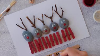 Çakıl taşları, deniz taşları, çamaşır mandalları ve beyaz arka planda dallardan oluşan kartpostalda Mutlu Noeller geyiği yapmak. Doğal Eko tarzı diy. Hediye fikri. Adım adım. Üst görünüm.