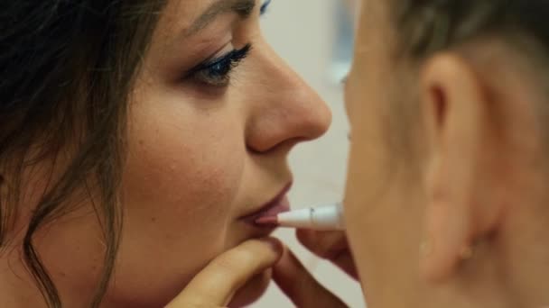 Maquiagem artista aplicando batom. close-up dos lábios de uma jovem mulher, artista de maquiagem profissional com uma escova aplica batom cor natural. moda nos bastidores. — Vídeo de Stock