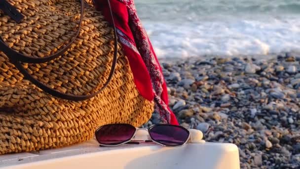 海の波を背景にサンラウンジャーの端にサングラスやバッグ。夏休みだ。サングラスはビーチの白いサンラウンジャーに横たわっています. — ストック動画