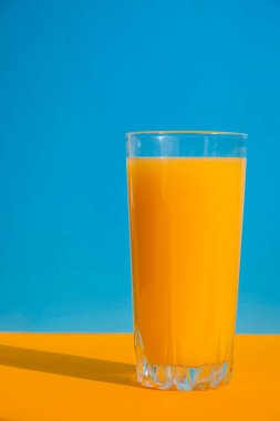 Mavi ve sarı arka planda bir bardak taze sıkılmış portakal suyu. Meyve suyu, taze soğuk içecek. Yazın dinlenmek için. Boşluğu kopyala