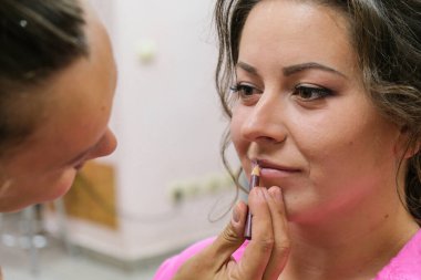 Makyöz genç bir kızın dudaklarını boyuyor. Geline makyaj yapan profesyonel bir makyöz.