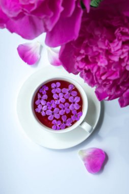 Pembe şakayık çiçekleri ve parlak masa üzerinde bir fincan çayla yaratıcı bir düzen. Bahar mevsimi sevgililer günü, kadın, anne, 8 Mart bayramı, romantik kahvaltı. Şık bir blog yazarı. Tebrik kartı. Davetiye. Günlük postası