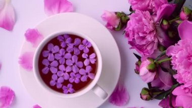 4k Rüzgârı pembe şakayık çiçekleri ve parlak masada bir fincan çay üflüyor. Bahar mevsimi sevgililer günü, kadın, anne, 8 Mart bayramı, romantik kahvaltı. Şık bir blog yazarı. Tebrik kartı