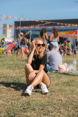 Festivalde çimlerde oturan genç bir kadın. Kız dışarıda eğleniyor, olumlu duygular ifade ediyor parkta eğleniyor. Milenyum kuşağı yaşam tarzı
