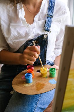 Çalışan yaratıcı bir ressam. Sanatçı işyeri, hobi, el sanatları aletleri. Sanatçı kadın tuval resmi. Atölyede profesyonel genç kadın ressam çiziyor. Boş zaman aktivitesi. Evde sanat
