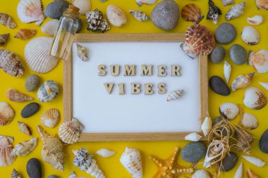 Kompozisyon kağıdı beyaz kağıt metin YAZI VİBES, deniz kabukları, çakıl taşları, sarı arka plan modeli. Boşluk, üst görünüm, durgun hayat, düzlük. Deniz seyahati konsepti turizm ve tatil beldeleri. Yaz tatili
