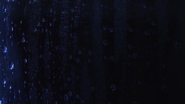 창문 유리에 빗방울 이 파란 빛으로 가까이 있어. 젖은 유리에 야간 조명 반사. 물방울의 배경 질감 — 비디오