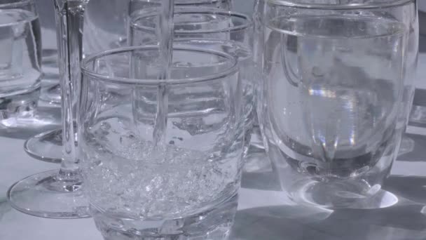 Water gieten Prachtige verschillende glazen staan op witte achtergrond in het zonlicht en creëren schaduwen. Hard licht, lange schaduwen. Creatief abstract concept van dranken, alcoholcocktails. Glaswerk — Stockvideo