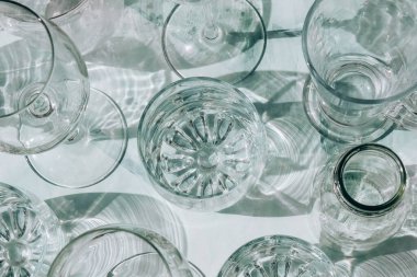 Güneş ışığında beyaz arka planda duran farklı güzel gözlükler gölgeler yaratır. Sert ışık, uzun gölgeler. Yaratıcı içki konsepti, alkol kokteyli. Cam kaplama konsepti. Geometrik şekiller