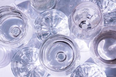 Güneş ışığında beyaz arka planda duran farklı güzel gözlükler gölgeler yaratır. Sert ışık, uzun gölgeler. Yaratıcı içki konsepti, alkol kokteyli. Cam kaplama konsepti. Geometrik şekiller