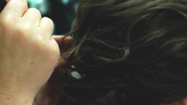 Penteado com spray de cabelo, preparação para o baile. Vista close-up de cabeleireiro estilista fazendo penteado usando pinças de ondulação para cabelos longos de mulher irreconhecível no salão de beleza. — Vídeo de Stock