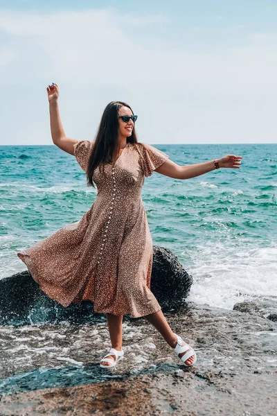 Plajda gökyüzüne karşı poz verirken giyinen ve su sıçratan bir kadın. Deniz manzaralı. Yaz tatili konsepti — Stok fotoğraf