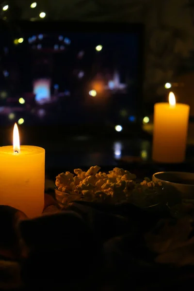 Filme no laptop à noite no quarto iluminado com velas. Pipocas. Ambiente de outono em casa — Fotografia de Stock