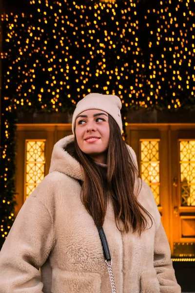 Young beautiful woman walking in new year decorated street market outdoor. Atmosphere of traditional Christmas market. Portrait of the young woman with bokeh lights — Stock Photo, Image