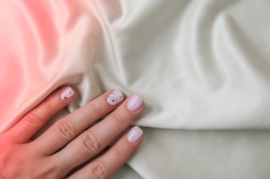 Kumaş ipeği arka planında zarif pastel doğal modern tasarım manikürü. Kadın eli işte. Jel tırnaklar. Çıplak manikür. Bej rengi. Temiz cilt. Spa salonu, reklam. Cilt bakımı. Güzellik. Tırnak bakımı. Güzellik tedavisi. Boşluğu kopyala