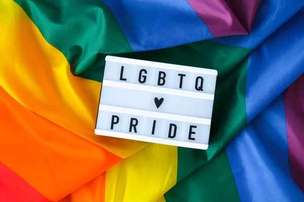 ライトボックスとテキストLGBTQ PRIDEとレインボーフラグ。シルク素材で作られたレインボーlgbtqフラグ。LGBTQプライド月間のシンボル。平等な権利。平和と自由 — ストック写真