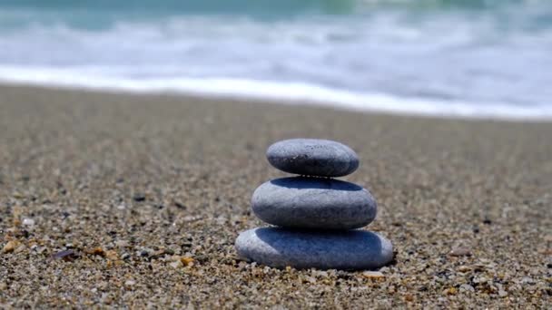 Скала балансирует на берегу океана. Пирамида гальки на песчаном берегу. Стабильная куча или куча в мягком фокусе с боке, закрыть. Дзен баланс, минимализм, гармония и мир — стоковое видео